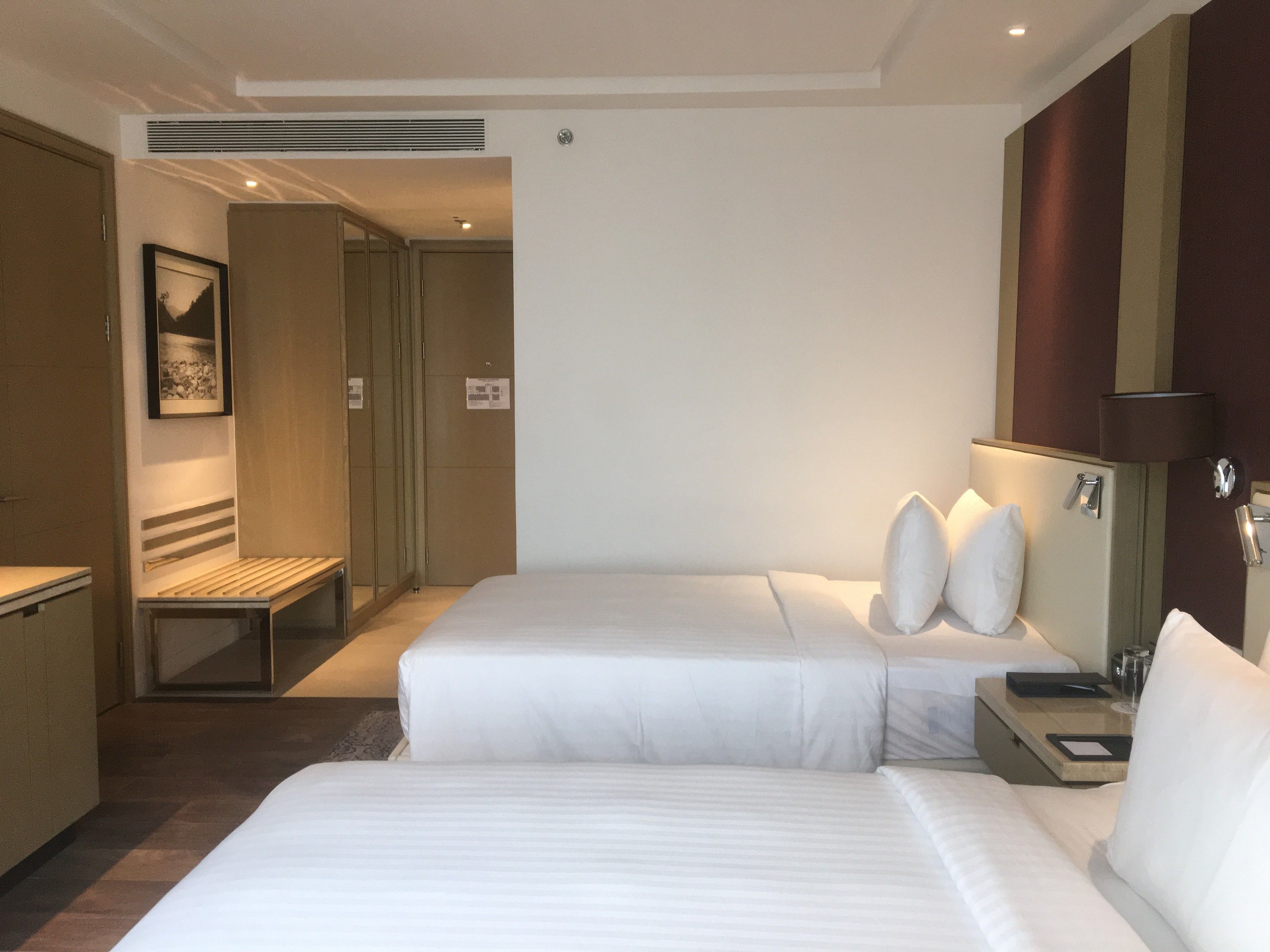 A hotel room with two beds, a bedside table, a lamp, a picture on the wall, and a door leading to a bathroom.
