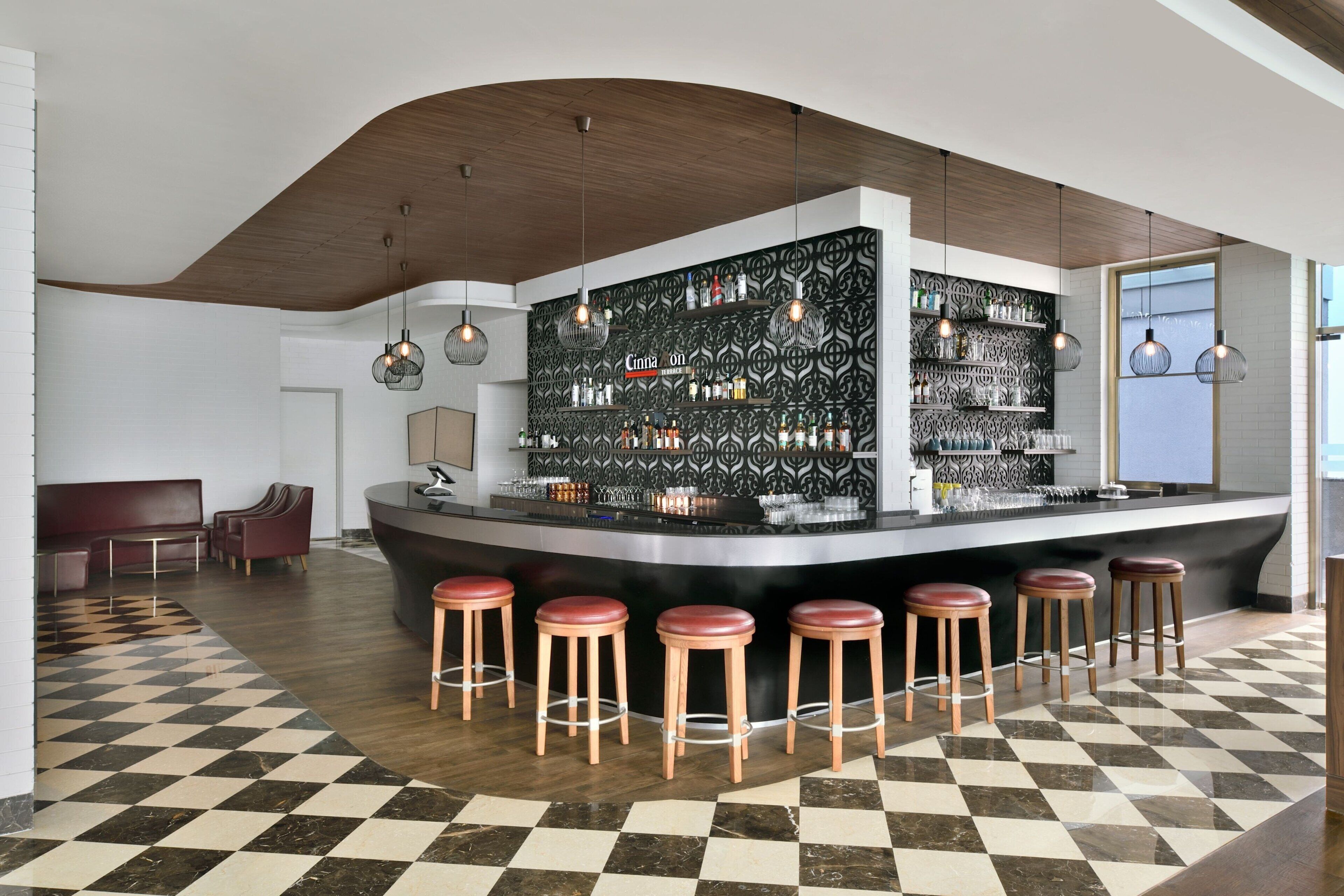 Un área de bar moderna con suelo a cuadros, techo de madera y taburetes.