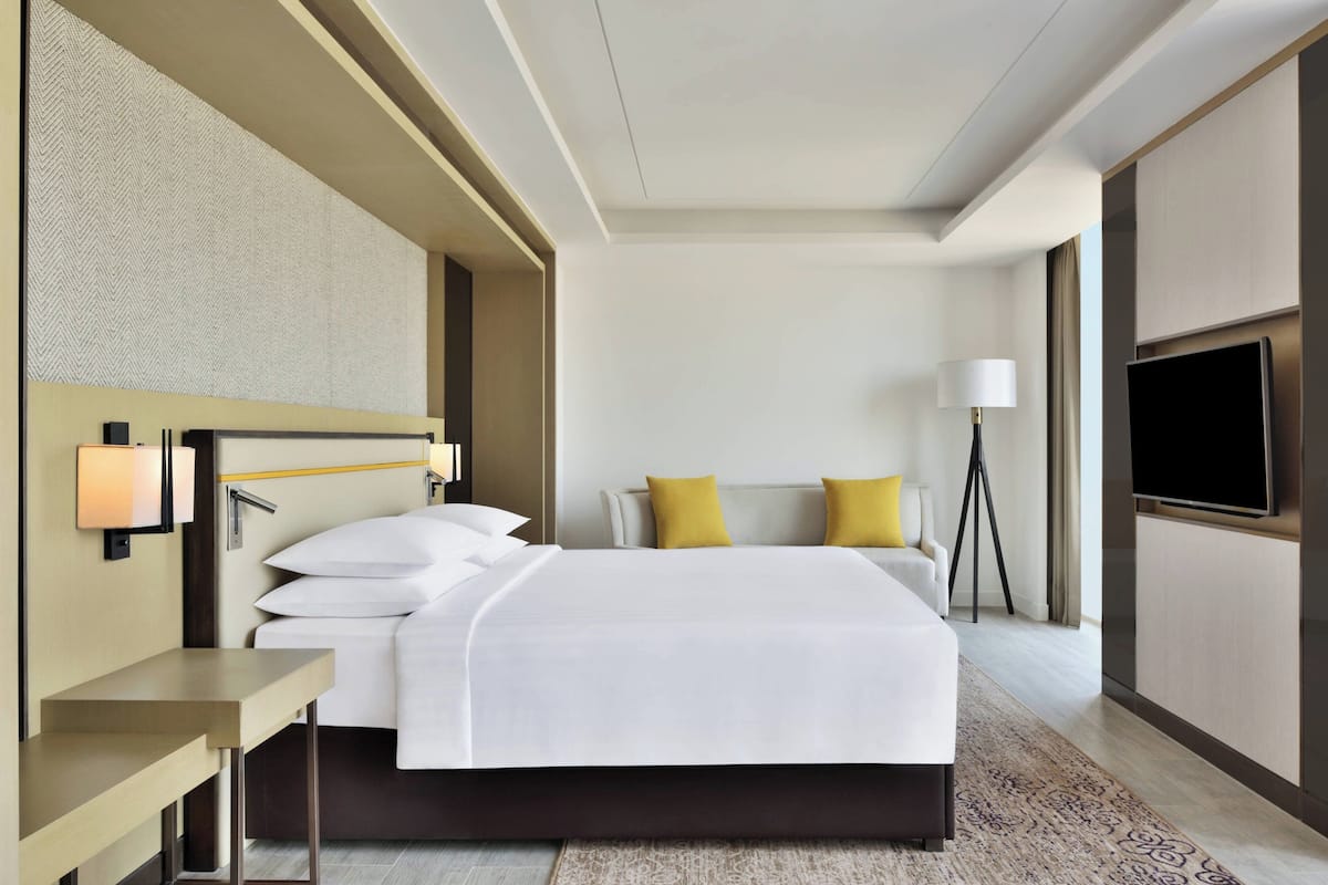A hotel room with a bed, bedside table, lamp, TV, and a patterned wall.