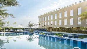 Un hotel moderno con piscina, sillones de descanso y un edificio con ventanas grandes.