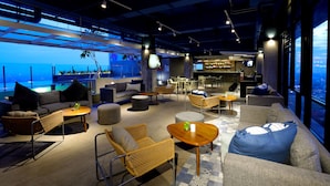 A modern lounge area with sofas, chairs, and tables, featuring a bar and large windows with a city view. - The Zuri Pekanbaru (Pekanbaru)