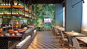 A restaurant with a tropical leaf wall, a buffet with various dishes, and a TV screen. - The Zuri Pekanbaru (Pekanbaru)