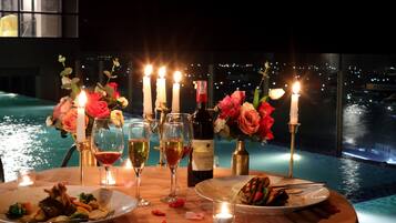 A romantic dinner setup by a pool with candles, flowers, and wine glasses.