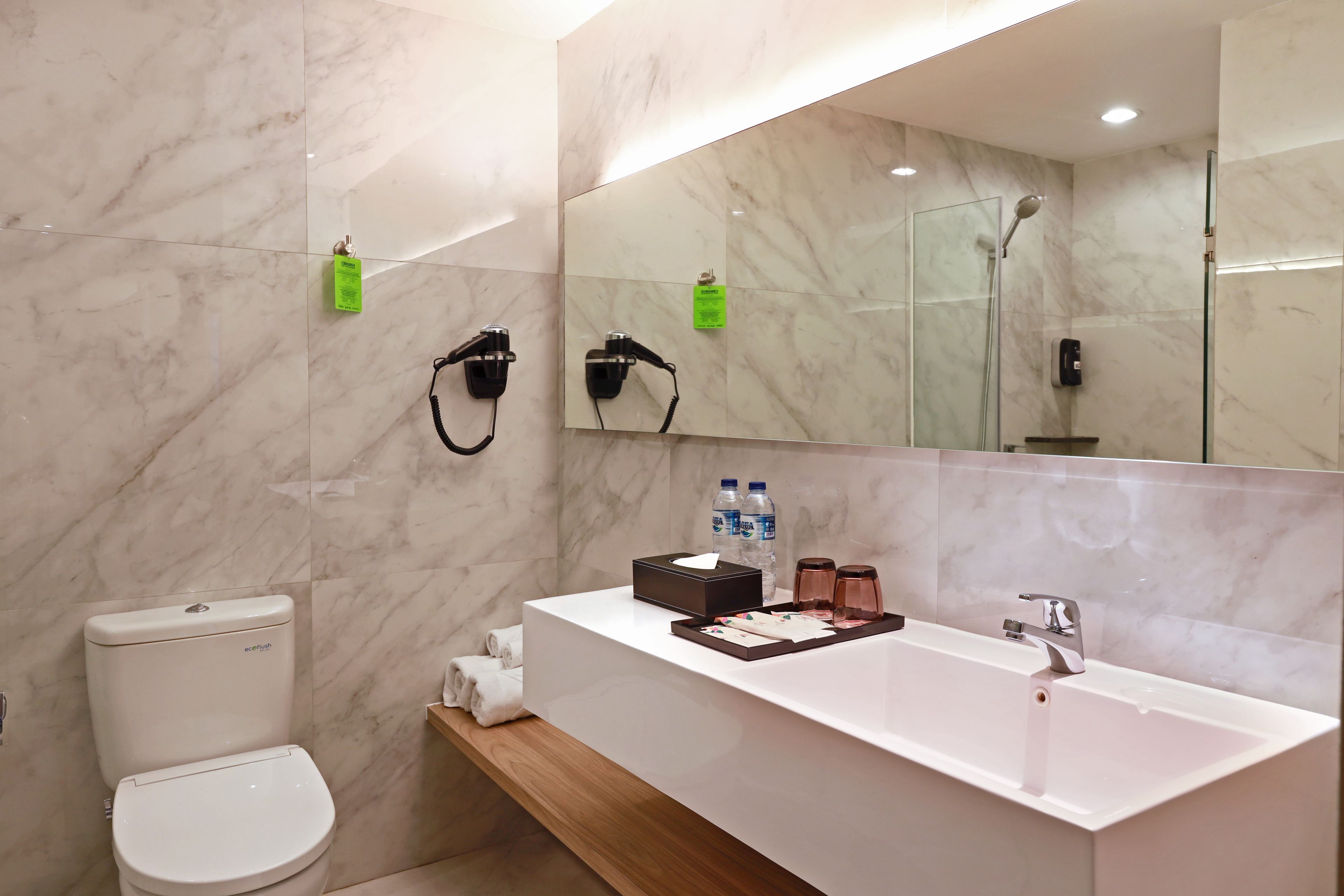 Een moderne badkamer met een wit toilet, een grote spiegel, een wastafel met een dienblad en een douchegedeelte.