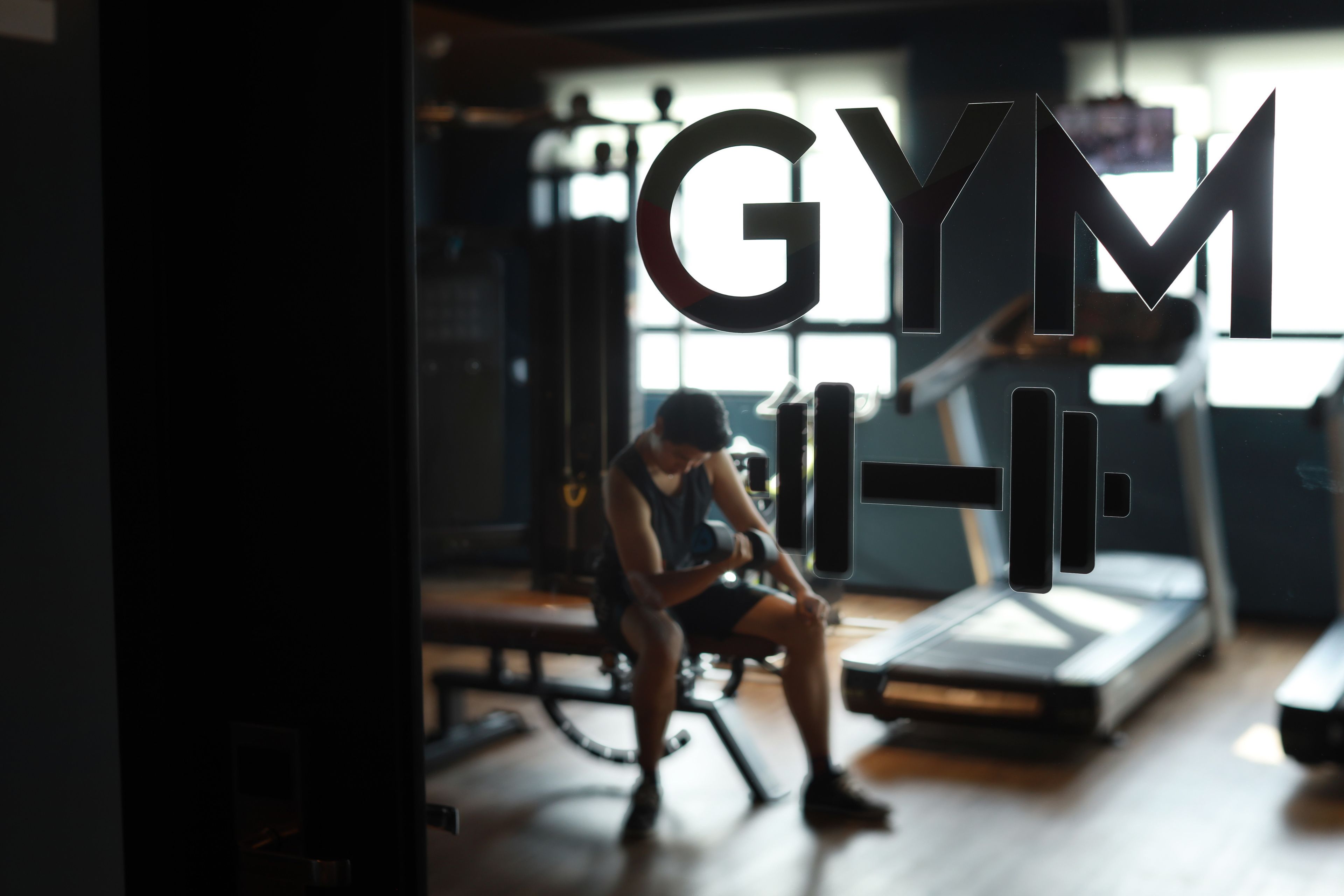 A gym with exercise equipment and a person sitting on a bench.