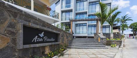 A modern hotel entrance with a stone facade, a sign reading "Azure Paradise," and a staircase leading to the entrance.