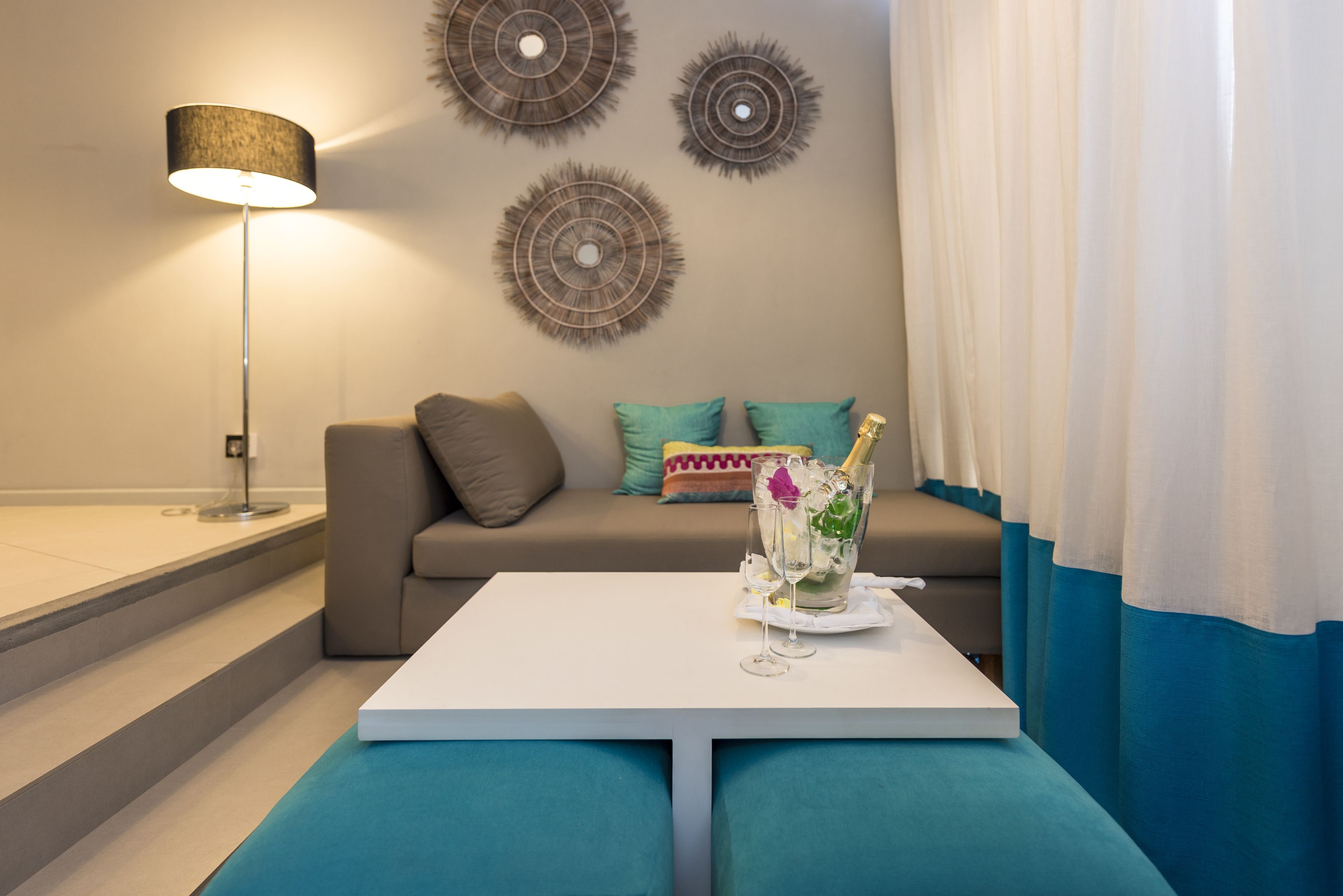 Una sala de estar moderna con una mesa blanca, cojines color turquesa, un sofá y decoración mural.