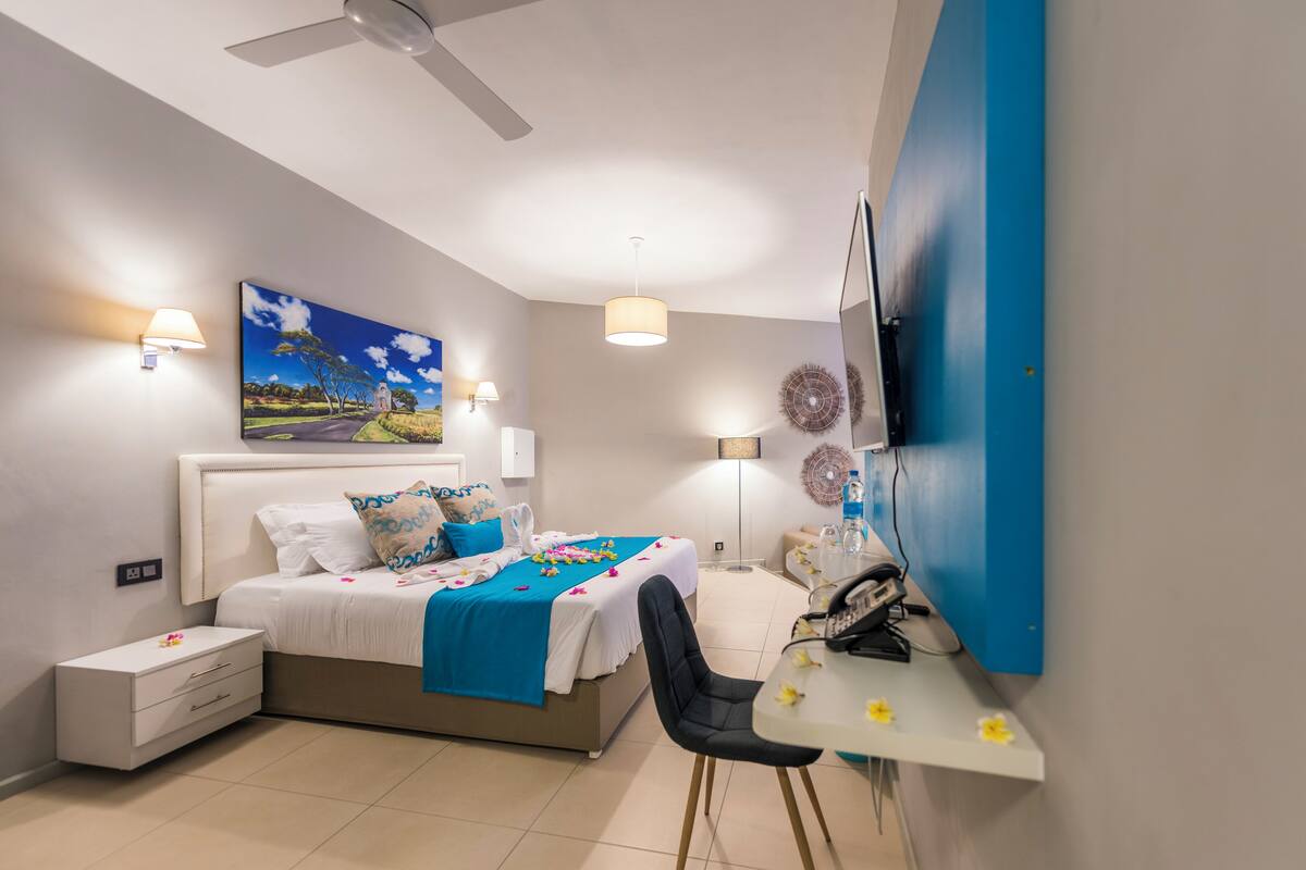 Quarto com cama, mesa de cabeceira, escrivaninha, cadeira, abajur e uma obra de arte na parede.