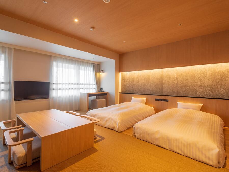 A modern hotel room with two beds, a wooden desk, and a large window with curtains.