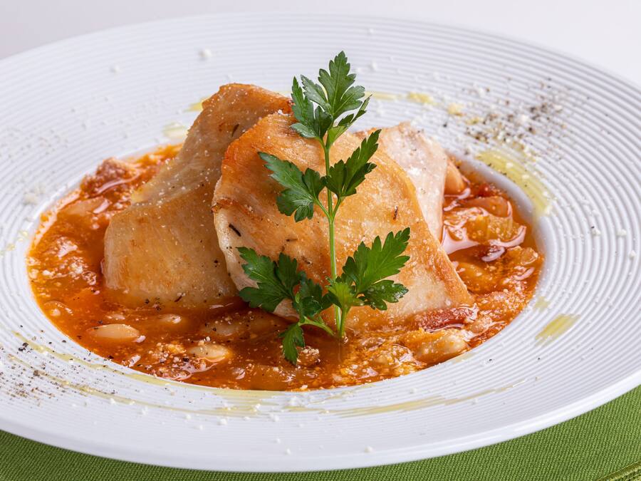 Un plato blanco con un guiso de pescado, adornado con perejil, sobre un mantel verde.