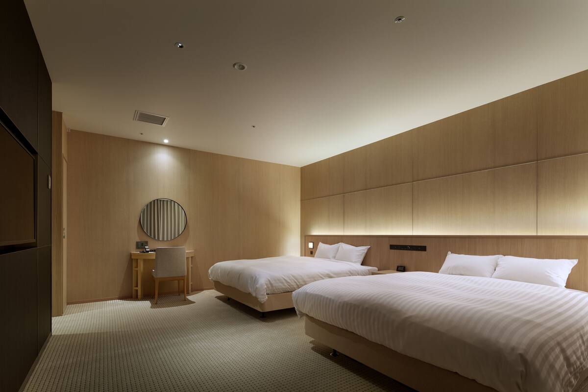 A modern hotel room with two beds, a desk, and a round mirror.