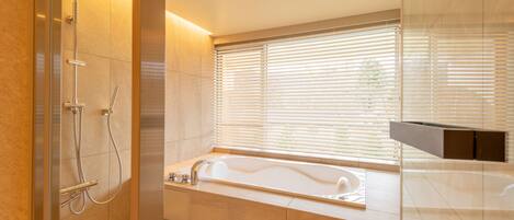 A modern bathroom with a glass-enclosed shower, a freestanding bathtub, and a window with blinds.
