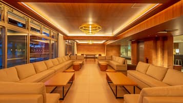 A modern lounge area with sofas, tables, and a central chandelier.