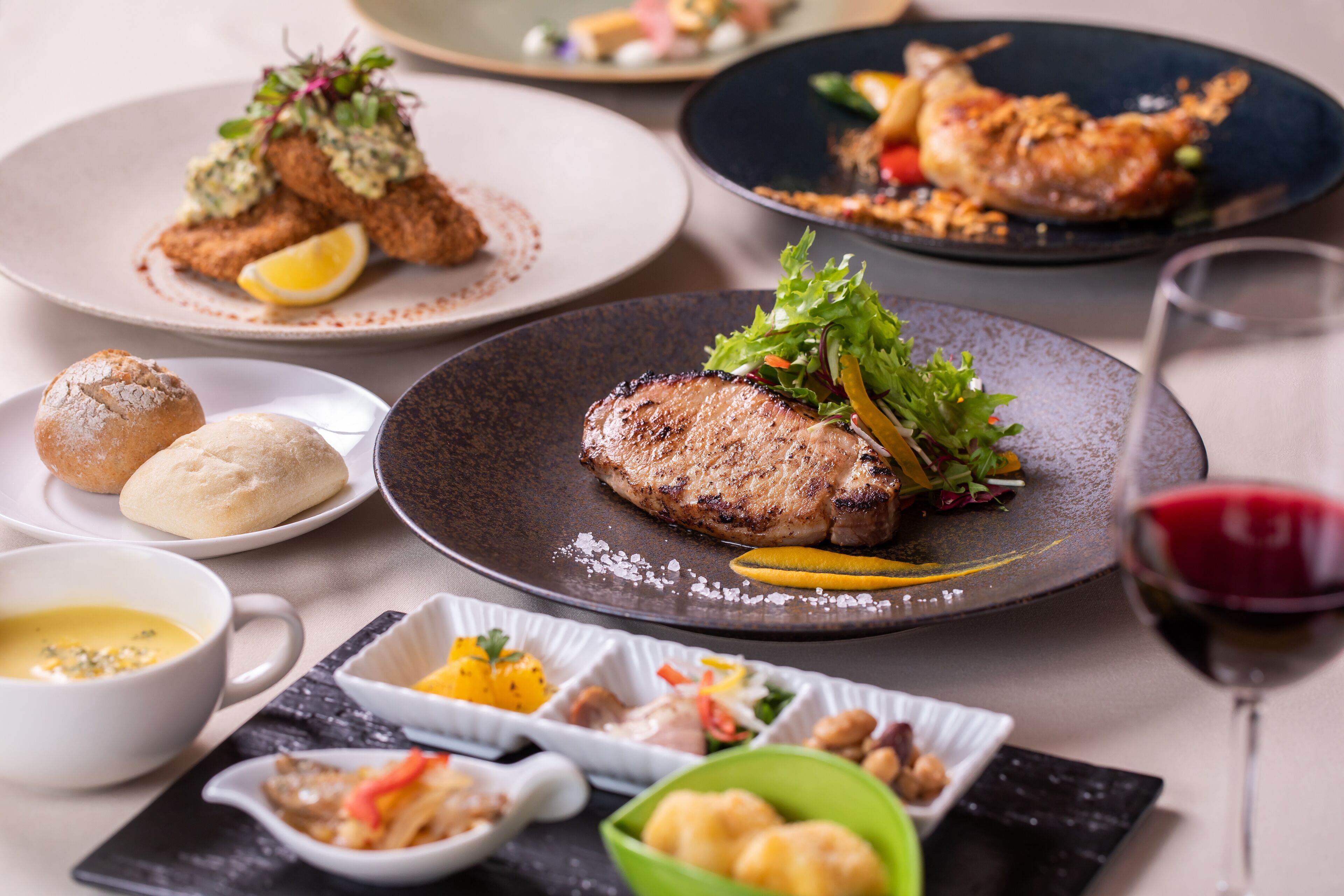 A variety of dishes on plates, including a grilled steak, bread, and a bowl of soup.