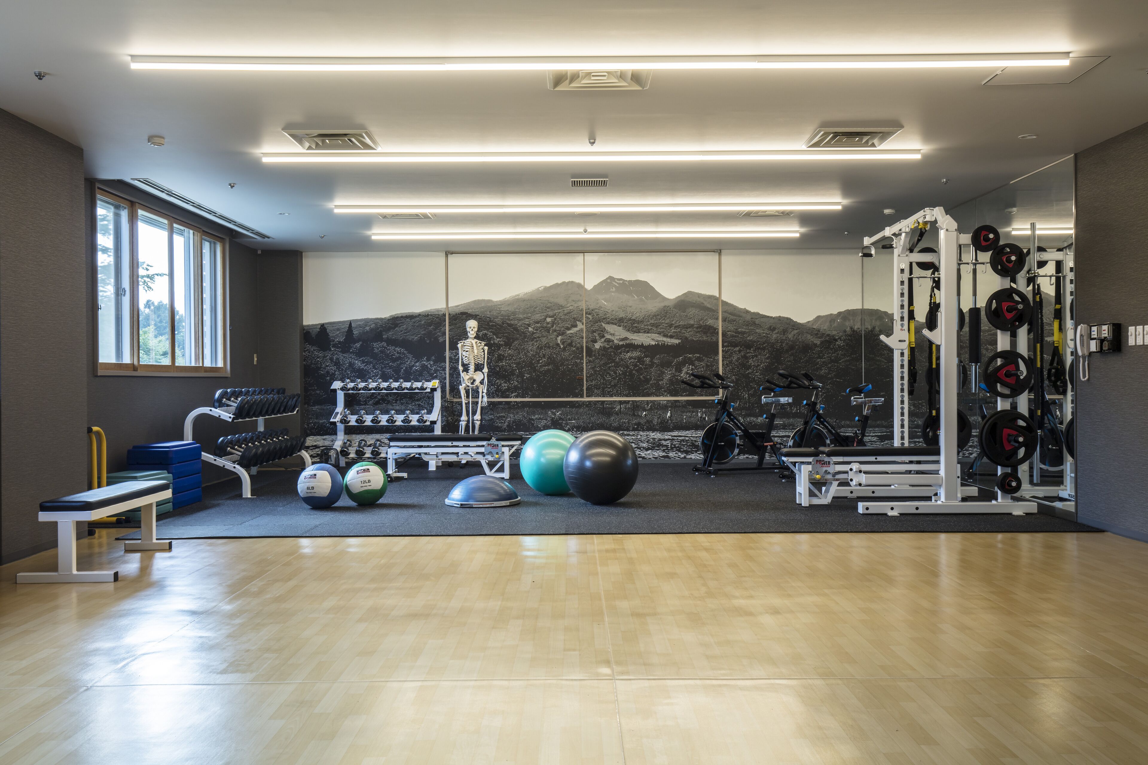 A gym with exercise equipment, a bench, and a large mirror reflecting a mountain view.