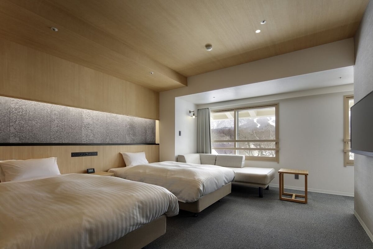 Ein Hotelzimmer mit zwei Betten, einem Schlafsofa, einem kleinen Tisch und einem großen Fenster.