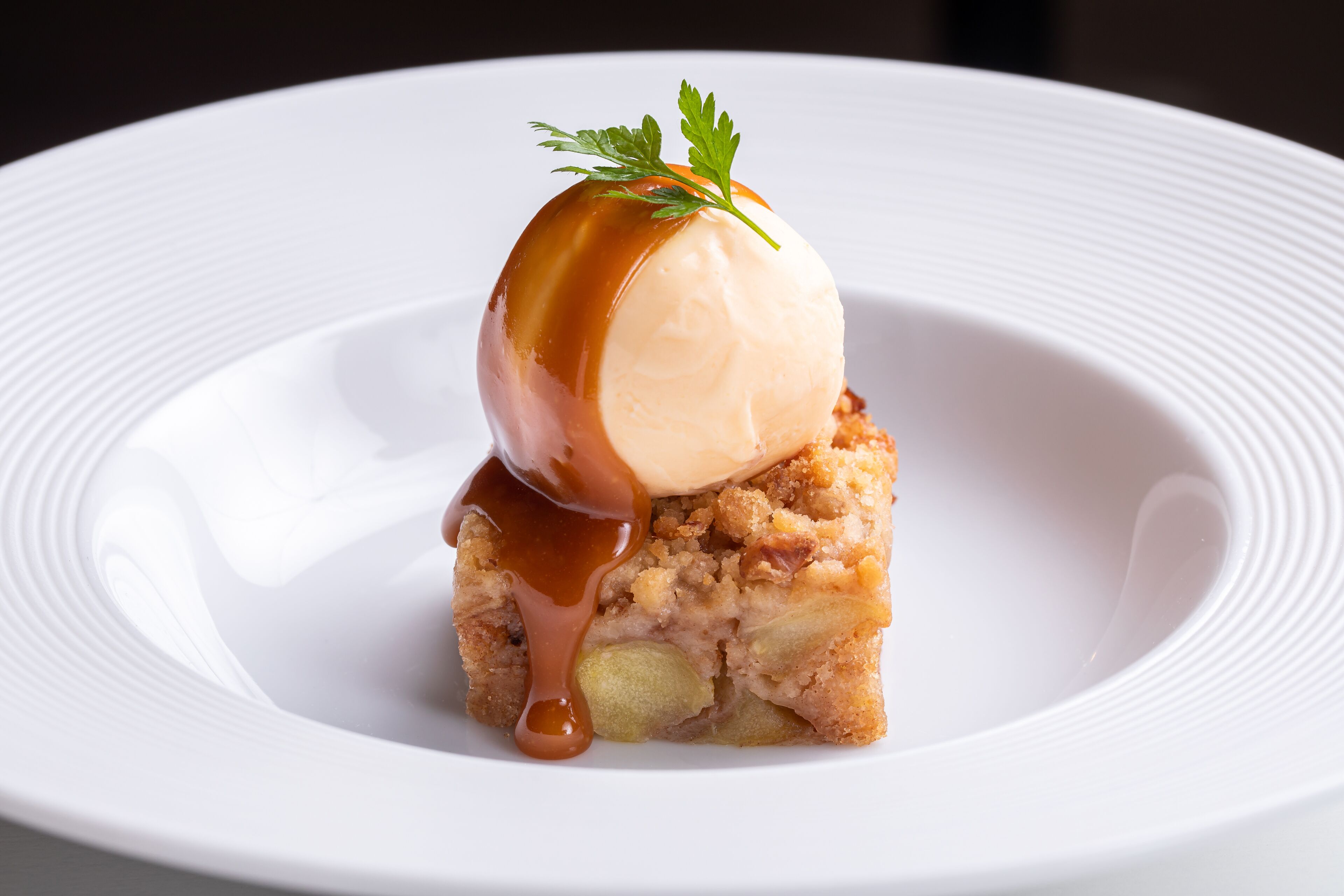 Un postre sobre un plat blanc, amb salsa de caramèl i guarnició.