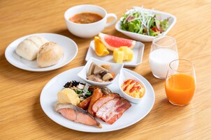 Una mesa de desayuno con diversos platos, incluyendo huevos, tocino, pescado y un vaso de zumo de naranja.