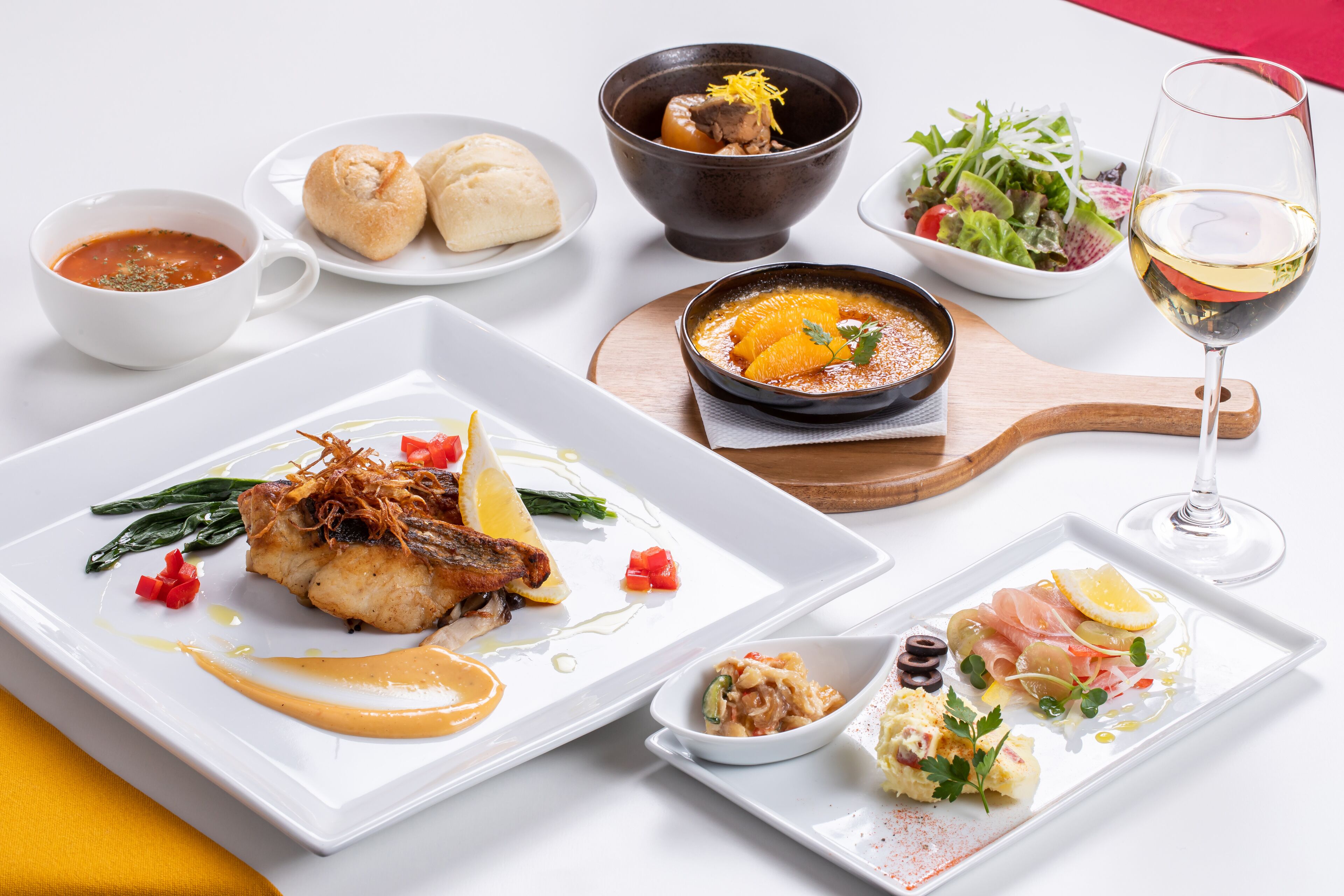 A variety of dishes on a white table, including a fish dish, a bowl of soup, and a salad.