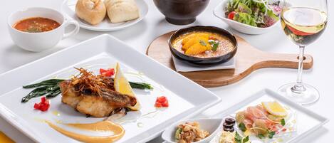 A variety of dishes on a white table, including a fish dish, a bowl of soup, and a salad.