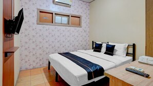 Ein Hotelzimmer mit Bett, einem an der Wand befestigten Fernseher, einem Fenster und einer Fernbedienung auf einem Holztisch.