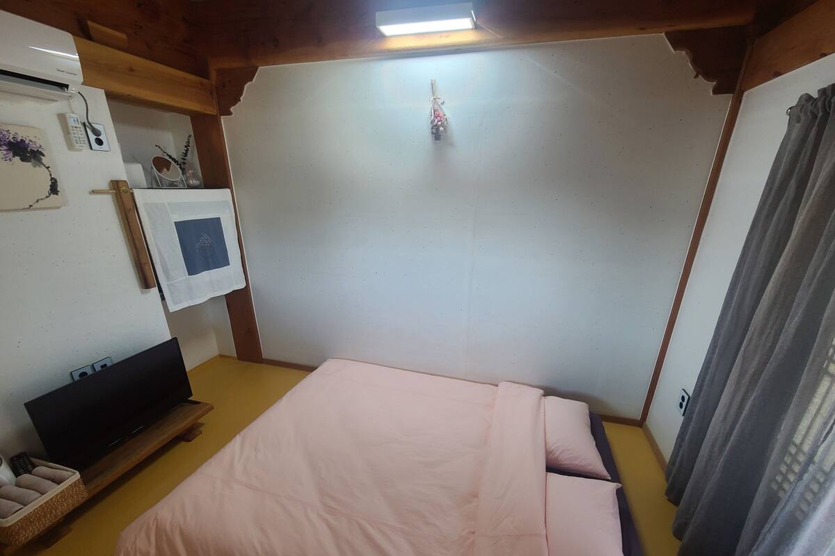 A bedroom with a bed, a TV, and a wall-mounted air conditioner.