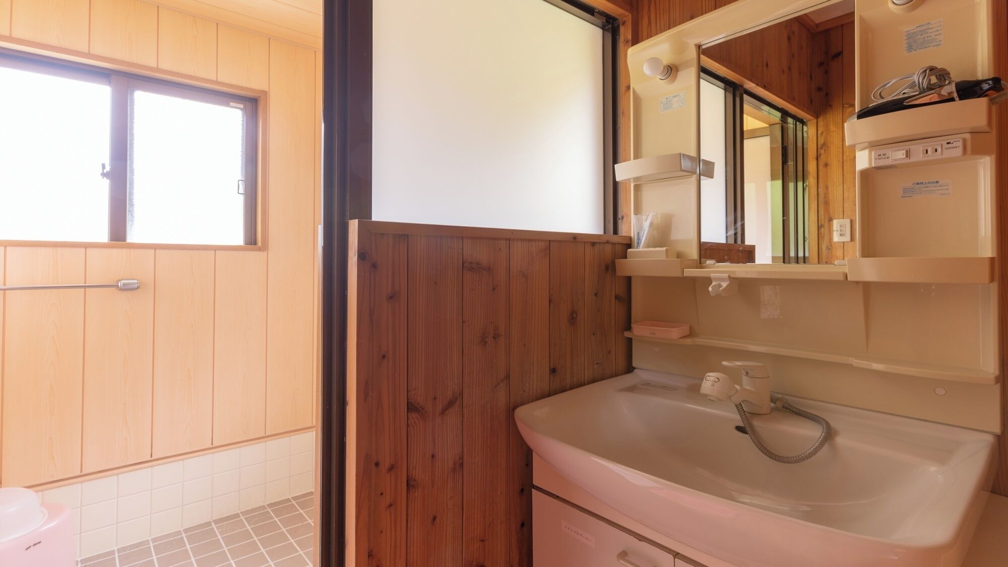 A bathroom with wooden paneling, a sink, a mirror, and a window.