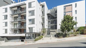 A modern multi-story building with balconies, a stone facade, and a clear blue sky.