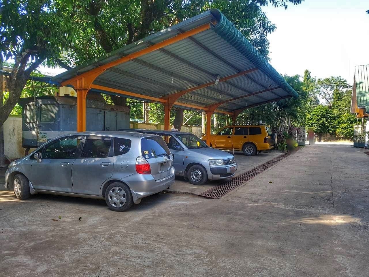A covered parking area with two cars parked under a metal roof.