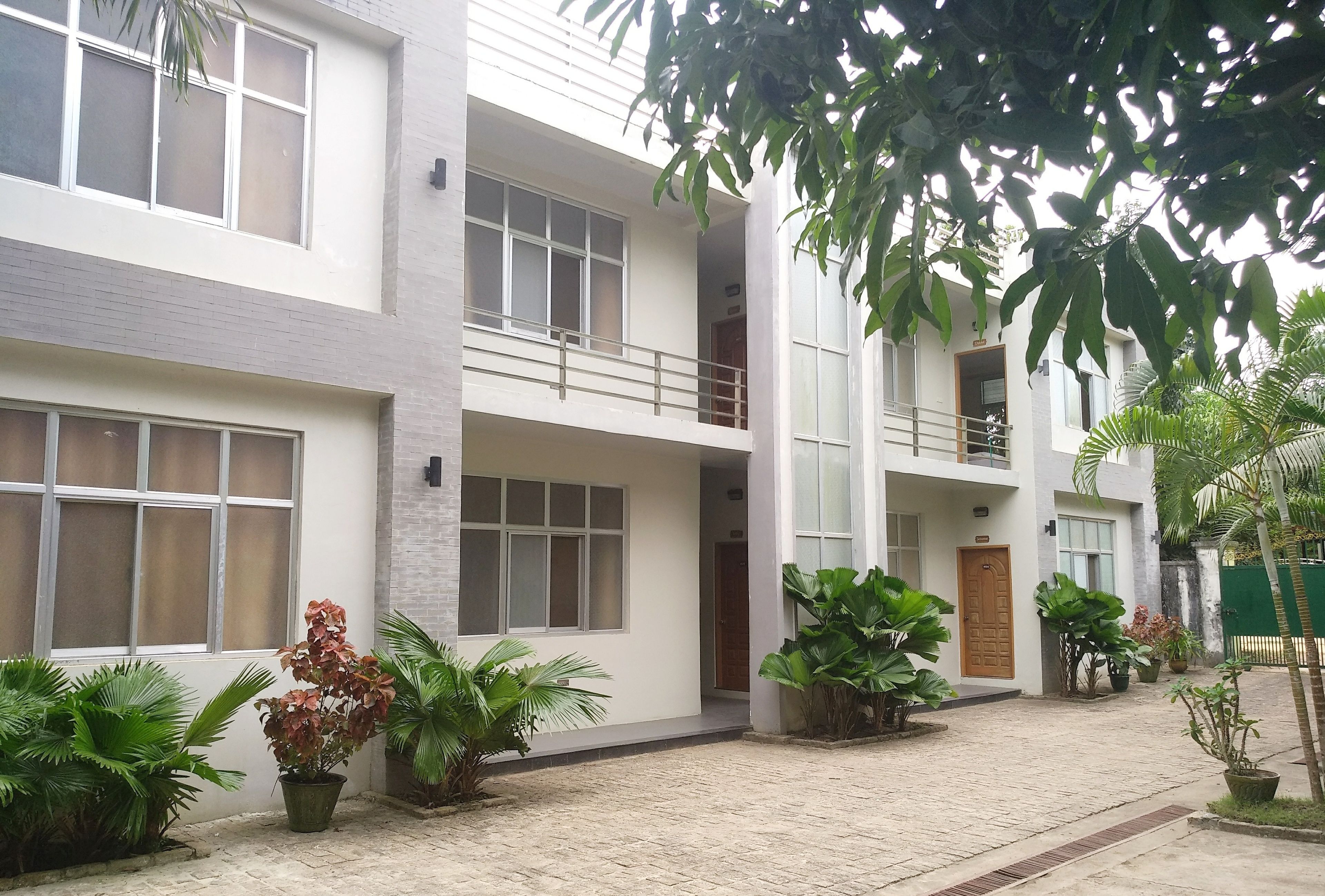 A modern building with multiple floors, large windows, and a paved courtyard with potted plants.