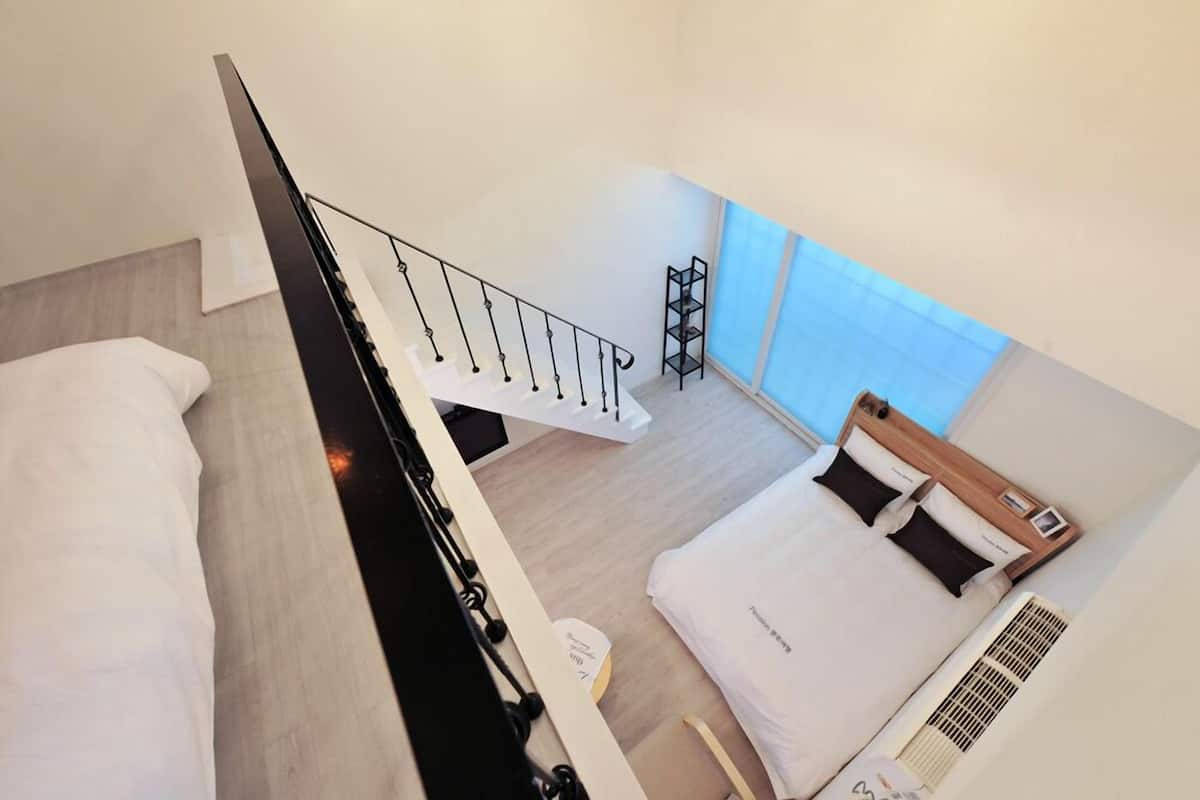 Una habitación de hotel moderna con una cama grande, un escritorio pequeño, una escalera y una ventana con vistas.