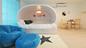 A modern room with a curved bed, a small table, two chairs, and a bean bag chair.