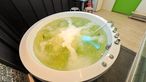 A large, round, white bathtub filled with green water and bubbles, with a single faucet.