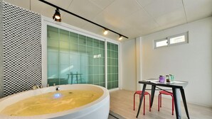 A modern bathroom with a large bathtub, a glass shower enclosure, and a small table with stools.