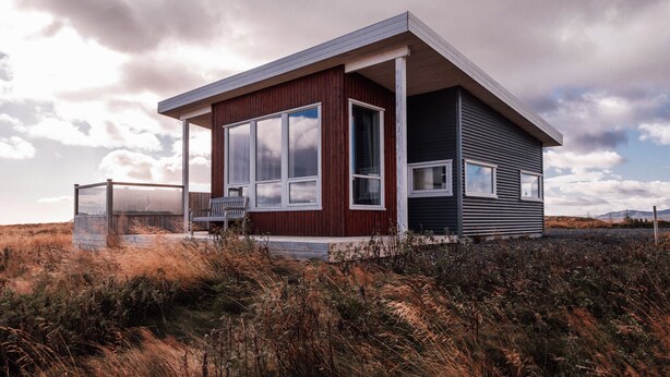 A modern house with a large window, a porch, and a view of the surrounding landscape. - Blue View Cabin 7A with Hot Tub (Bláskógabyggd)
