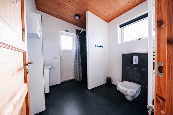 A compact bathroom with a white toilet, a small sink, and a shower area. - Blue View Cabin 7A with Hot Tub (Bláskógabyggd)