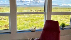 A room with a red chair, large windows, and a view of a grassy field. - Blue View Cabin 7A with Hot Tub (Bláskógabyggd)