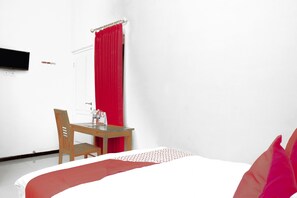 Una habitación de hotel con una cama, una mesa de madera, una silla, una cortina roja y un televisor de pantalla plana montado en la pared.
