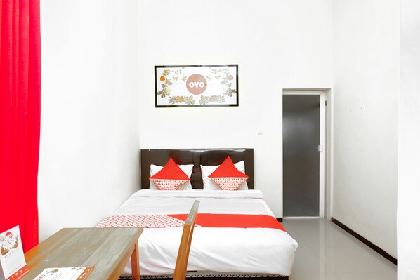 Una habitación de hotel con una cama, una mesa de madera, un cuadro en la pared y una cortina roja.