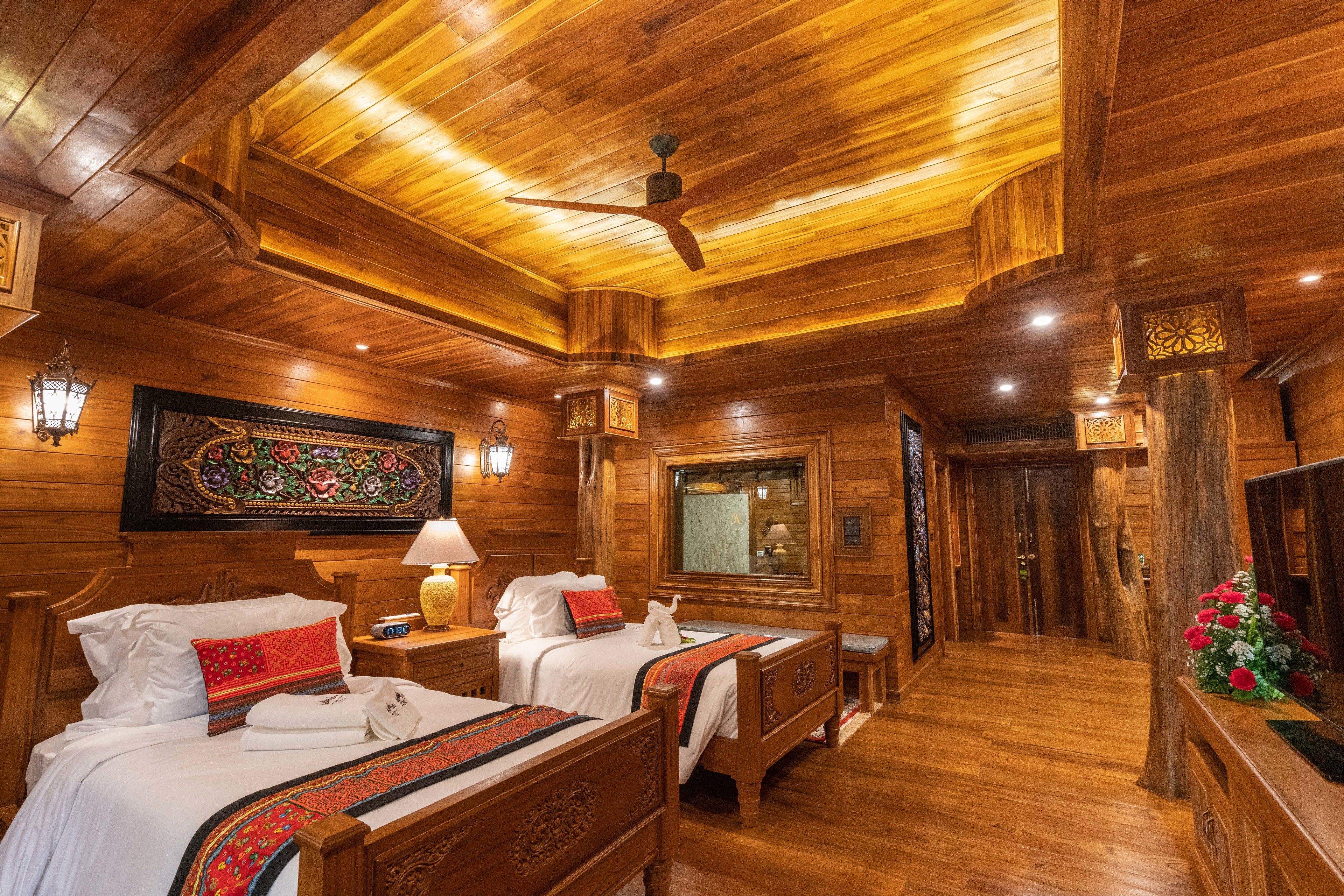 Habitación de hotel con decoración de madera, dos camas, ventilador de techo y un espejo grande.