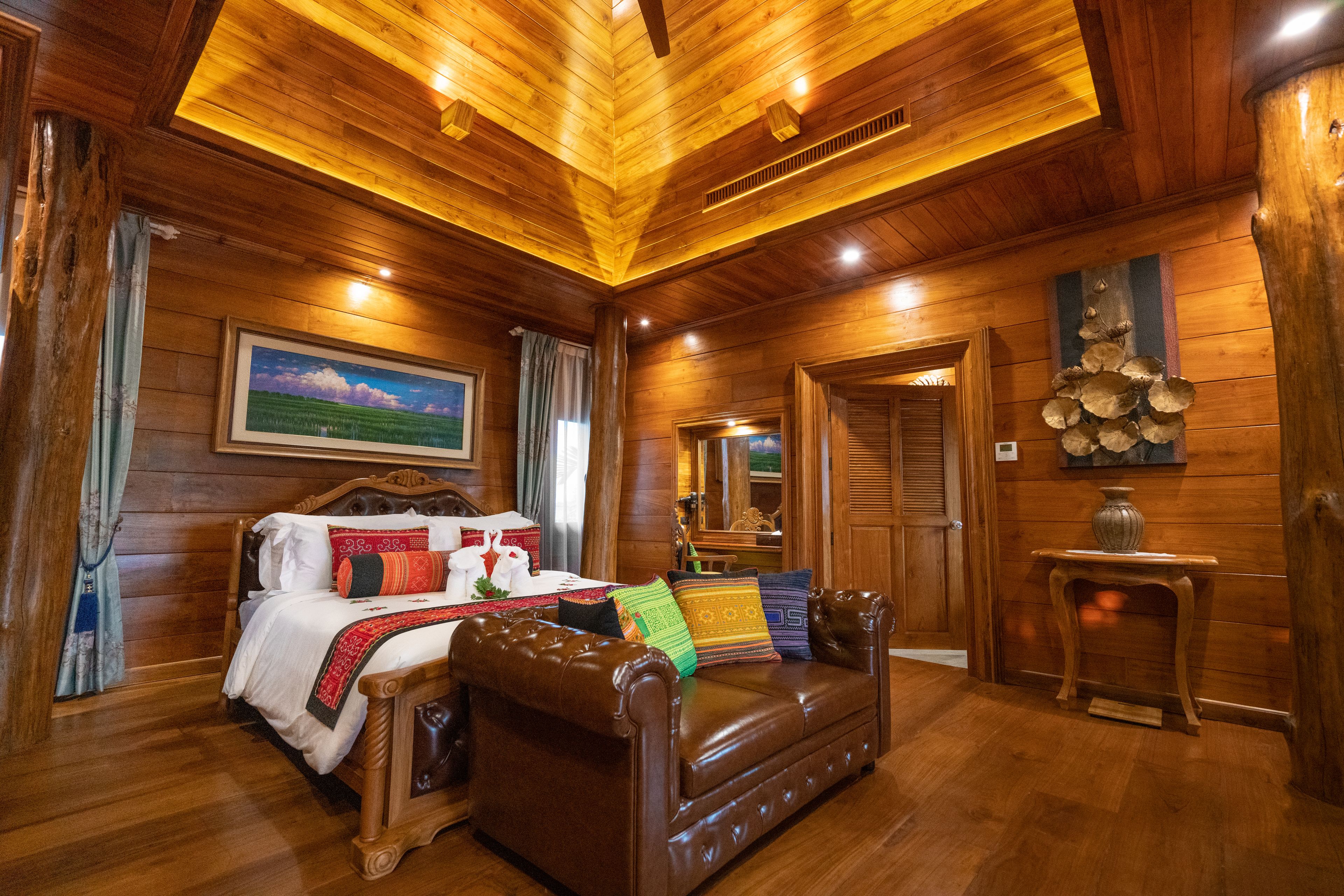 A wooden-paneled room with a bed, a leather sofa, a small table, and a mirror.