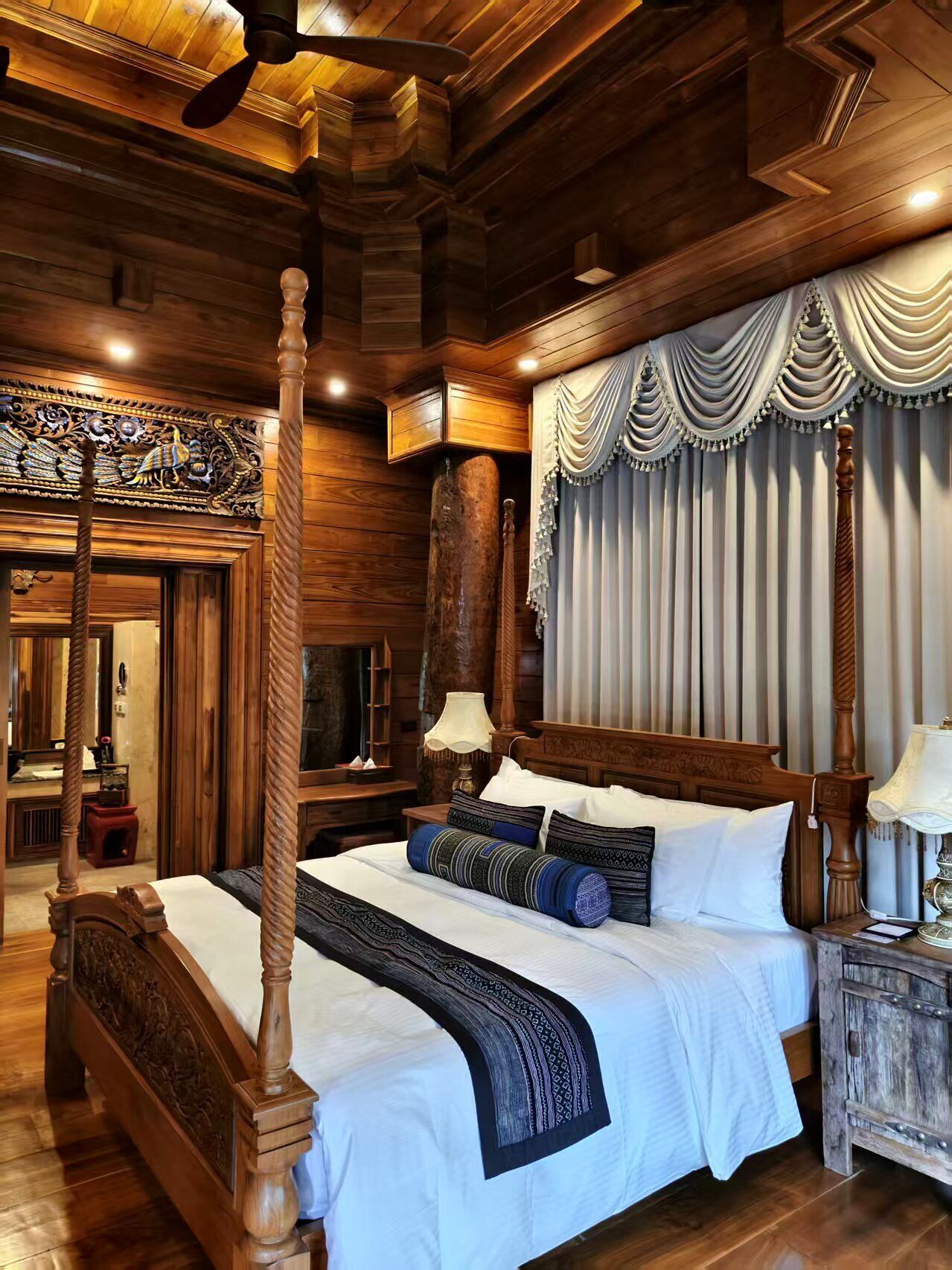 Una cama con dosel de madera, ropa de cama blanca y almohadas decorativas.