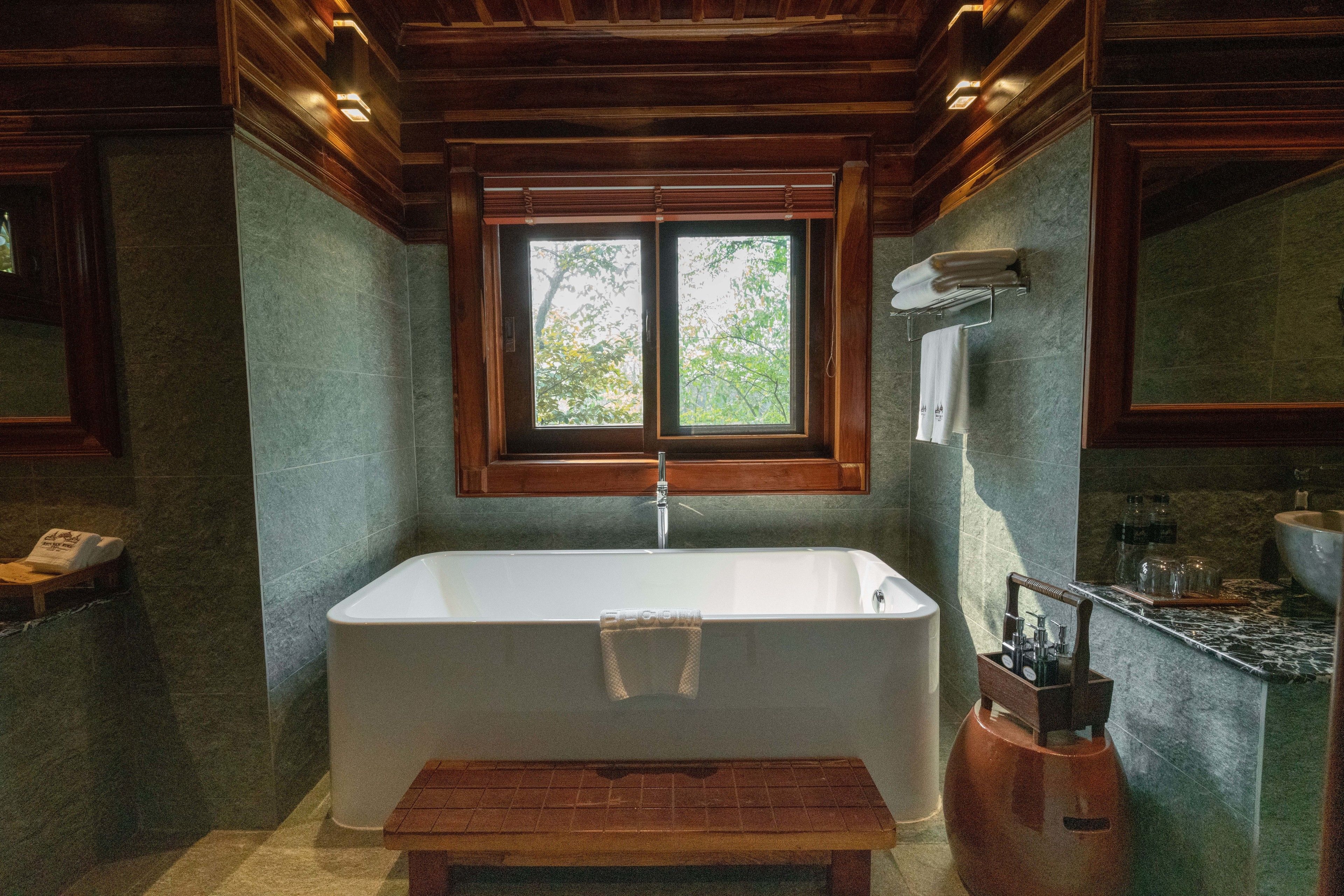 Une salle de bain avec une baignoire sur pieds, une fenêtre donnant sur la forêt et un banc en bois.