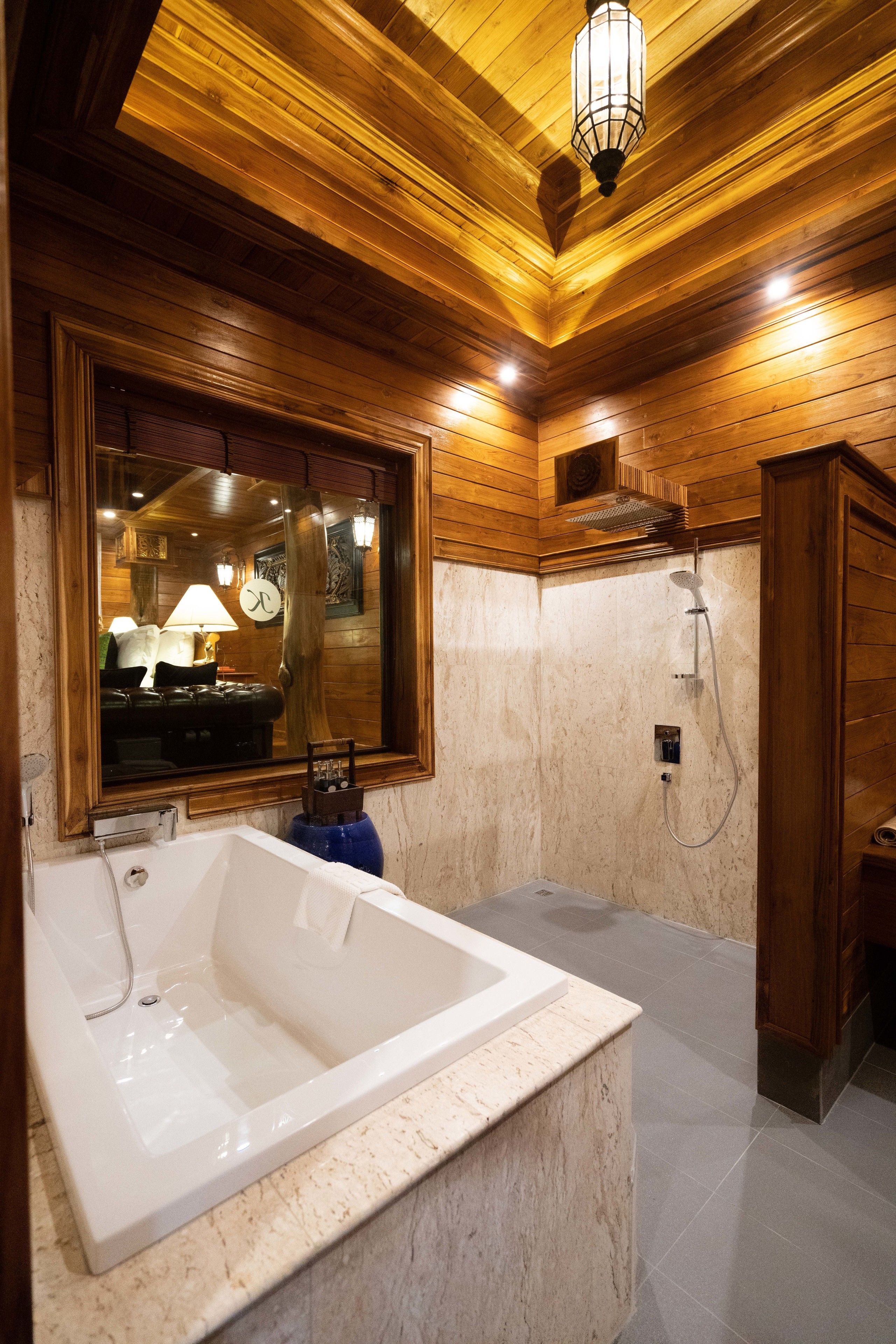 A bathroom with a large bathtub, wooden ceiling, and a mirror reflecting a room with a clock and lamp.