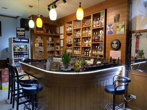 A bar area with a counter, stools, shelves of liquor bottles, and a sign indicating Wi-Fi availability. - Sue at Cozy Guesthouse (Karon)