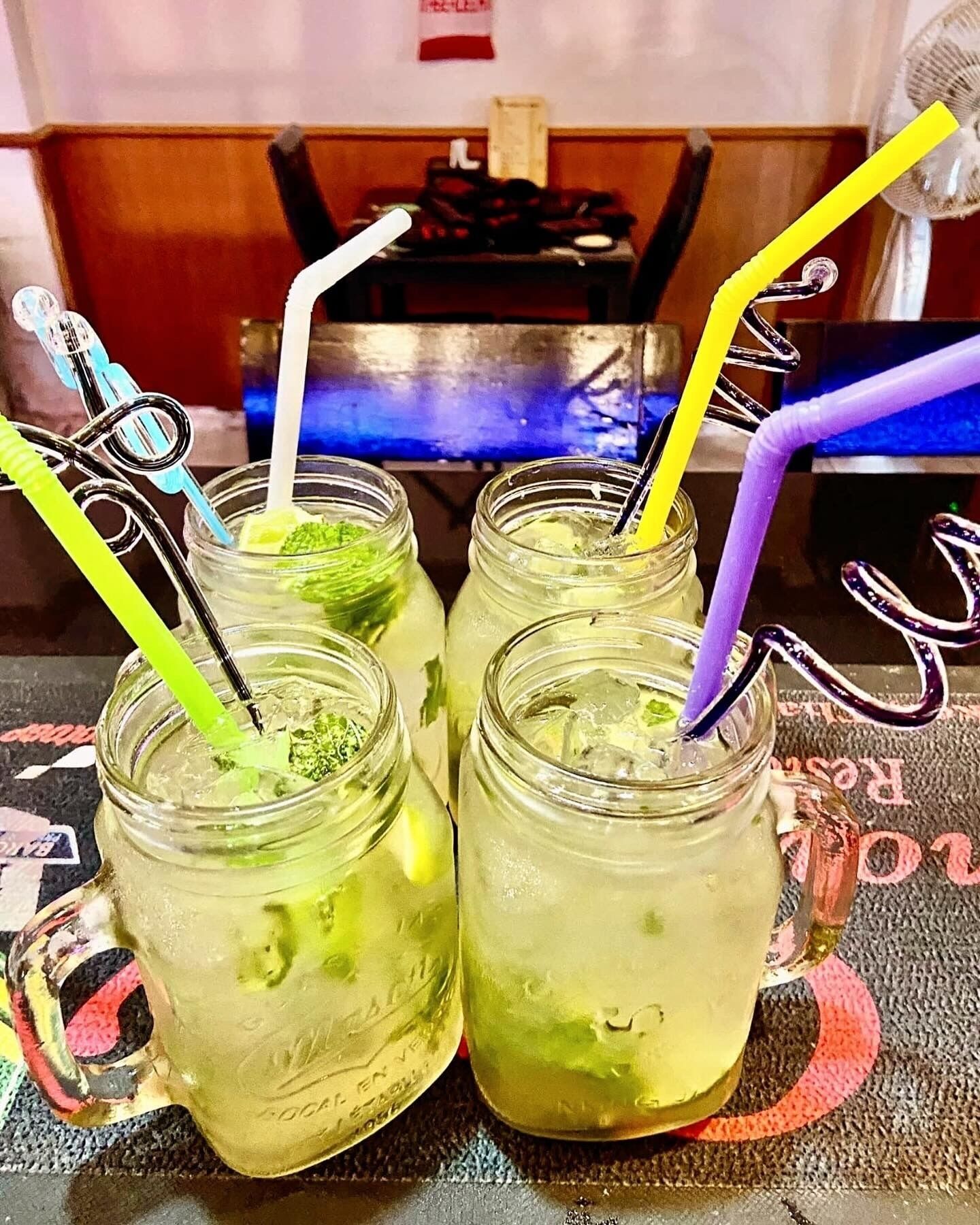 Vier Marmeladengläser mit Strohhalmen auf einem Tisch mit gemustertem Tischläufer.