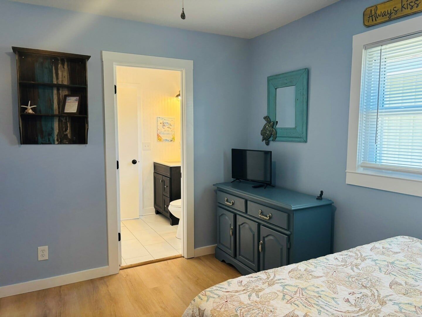 Une chambre à coucher comprenant un lit, une commode, un téléviseur et une porte donnant sur une salle de bain.