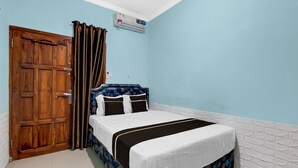 A bedroom with a wooden door, a bed with a floral headboard, and an air conditioning unit on the wall. - Hotel O near UGM formerly Bayang Brothers Guest House (Depok)