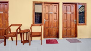 Un edificio con tres puertas de madera, cada una marcada con un número. Hay dos sillas de madera y una pequeña mesa frente a las puertas.