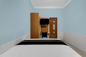 Un dormitorio con una cama, un escritorio con silla, un televisor y una puerta.